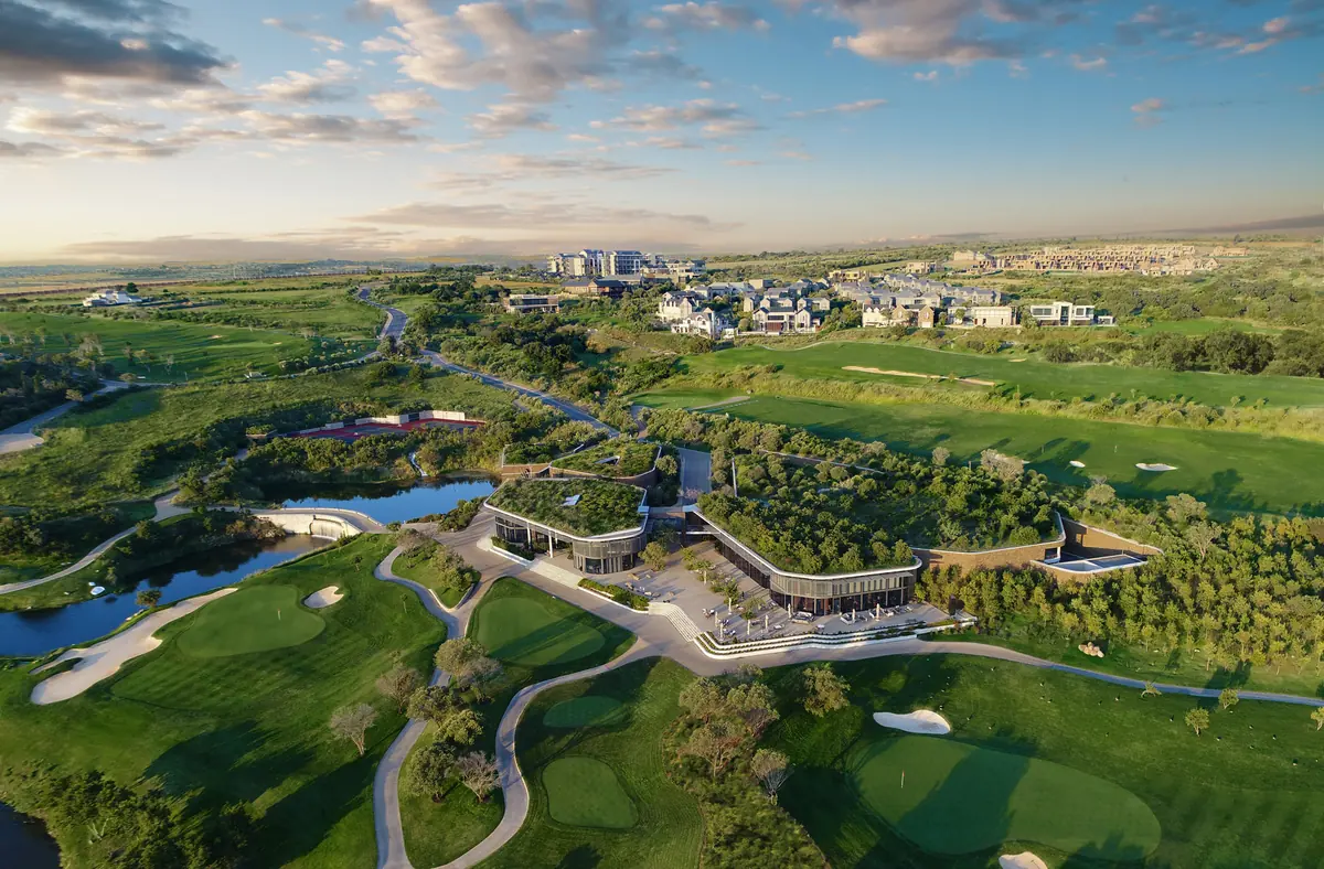 Aerial view of a golf clubhouse with a green roof, surrounded by fairways, greens and a lake