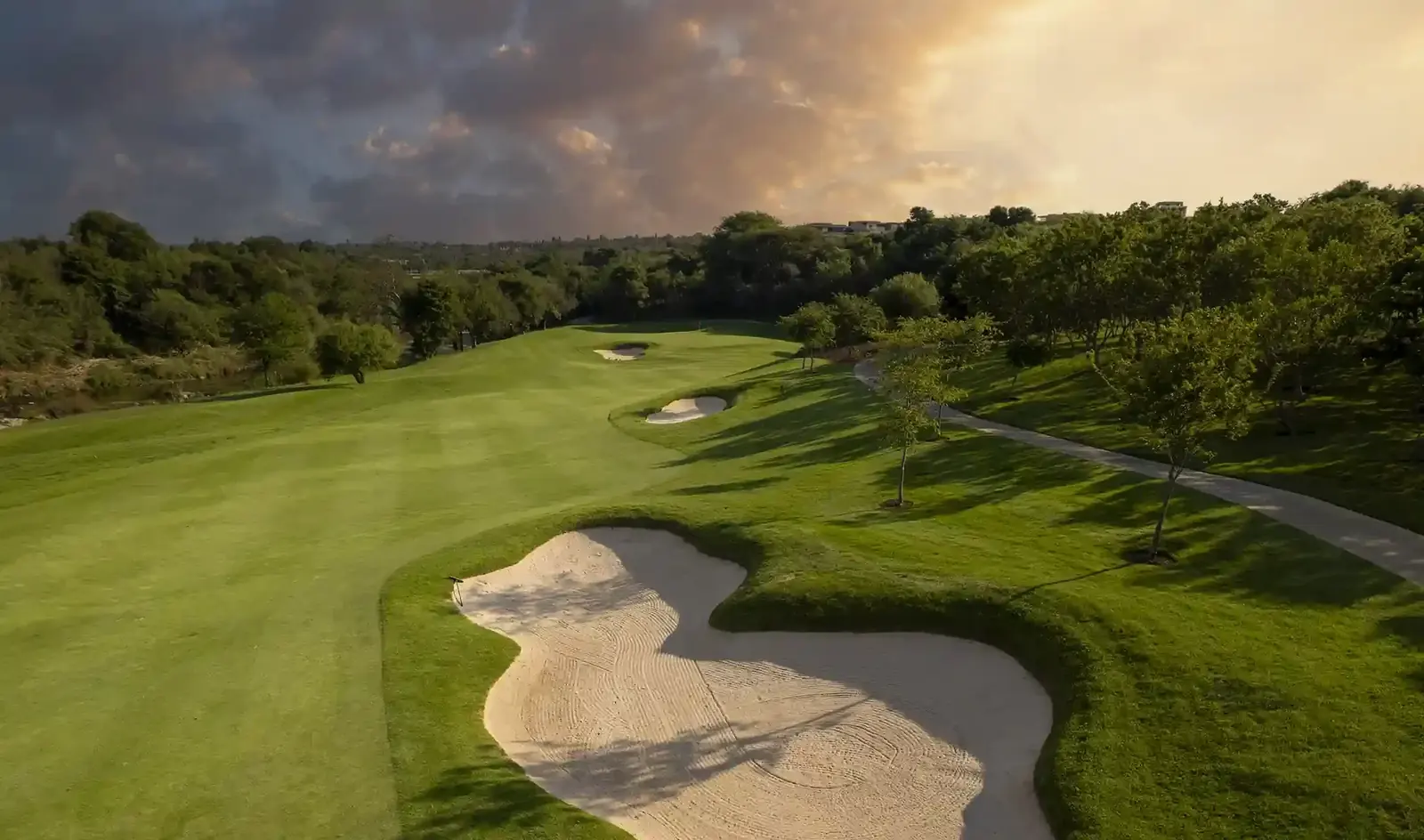 Golf fairway and sand bunkers framed by trees under a golden sunset sky